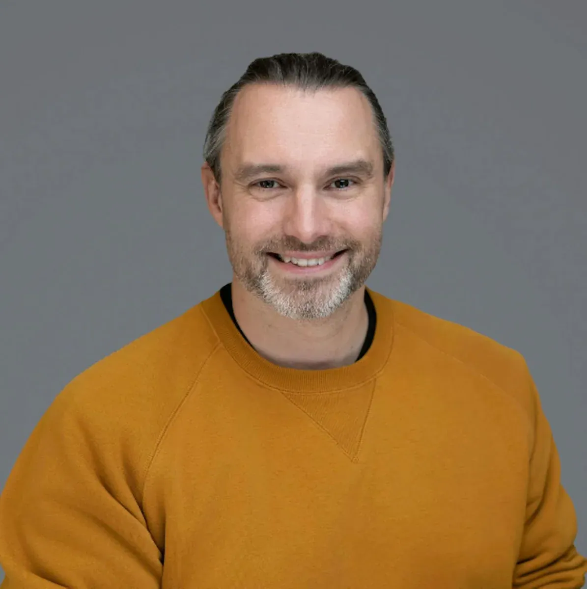 Sean Betts wearing a mustard-coloured sweatshirt against a grey background.
