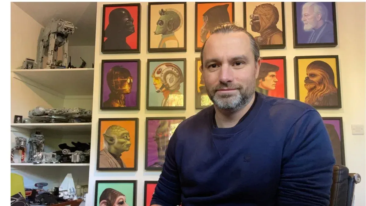 Sean Betts sitting in front of a wall of framed artwork.